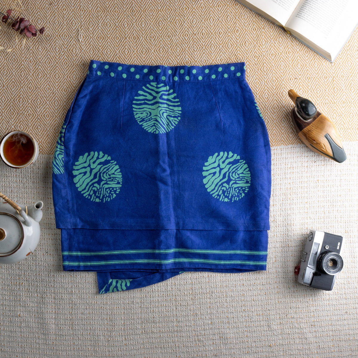back view Vintage Versus Versace 90s Linen Mini Skirt – royal blue linen with bold oversized green zebra-print medallion pattern, green polka dot waistband, wrap-style asymmetric front panel, green stripe hem border, Italian summer luxury, flat lay editorial shot