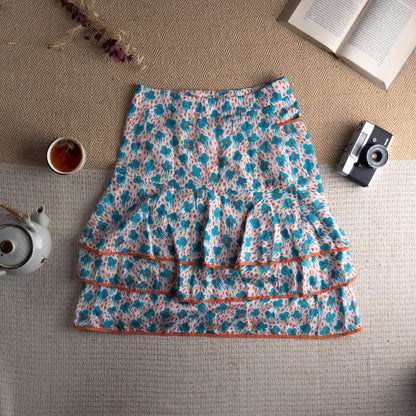 back view Cacharel Archival Deadstock Tiered Ruffle Skirt – white silk-cotton blend with all-over turquoise blue abstract daisy print and red dot scatter, drop waist with three red button front closure, small side pocket with orange trim, double tiered ruffle hem with orange grosgrain ribbon trim, coquette French chic quiet luxury, flat lay editorial shot