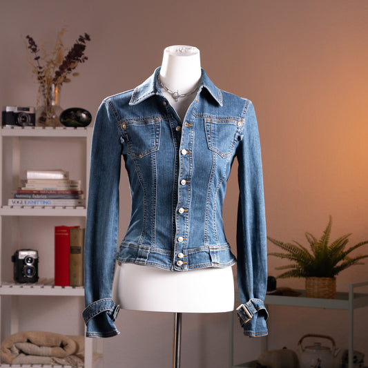 Archival Versace Y2K Denim Jacket – medium blue wash stretch denim with corset-stitched back seaming for a body-con silhouette, point collar, silver logo snap buttons, dual chest flap pockets, long sleeves with silver buckle cuff detail, Made in Italy by Ittierre, product shot on dress form