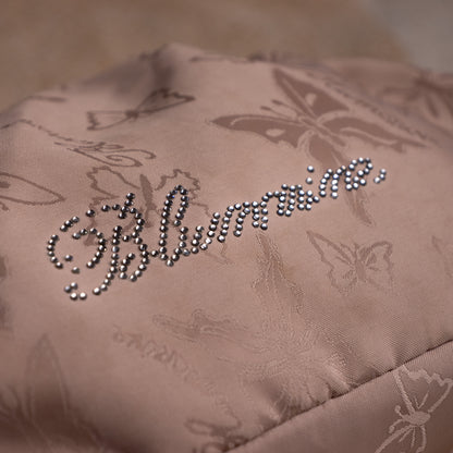 close up Blumarine Y2K Baguette Bag by Anna Molinari – blush beige nylon with tone-on-tone butterfly jacquard print, rhinestone crystal "Blumarine" script logo, dual rolled leather top handles with gold ring hardware, zip closure, Made in Italy, shown on dress form