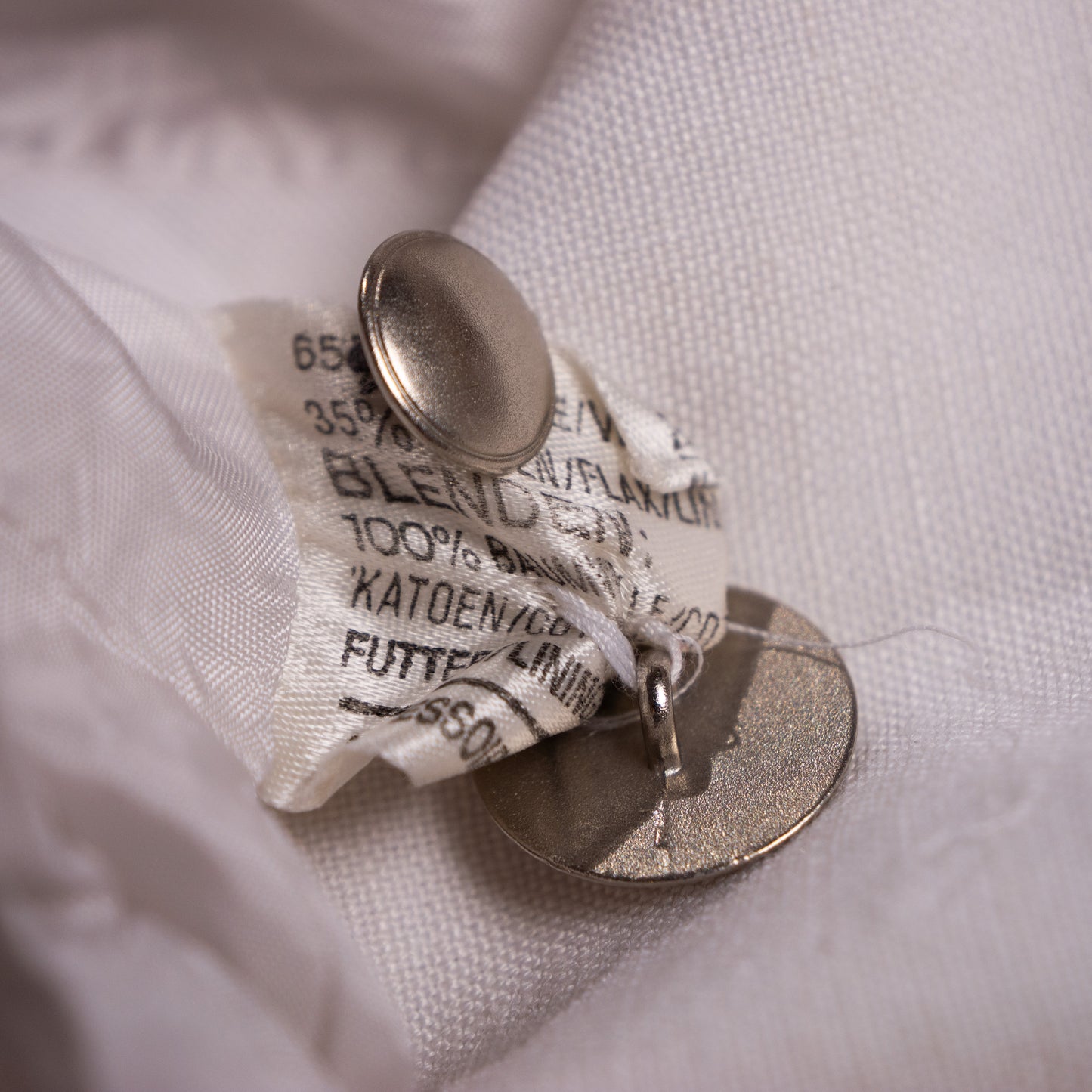 Authentic 1980s material composition tag showing 65% Flax-Linen and 35% Cotton blend next to the heavy custom-brushed metallic factory buttons.
