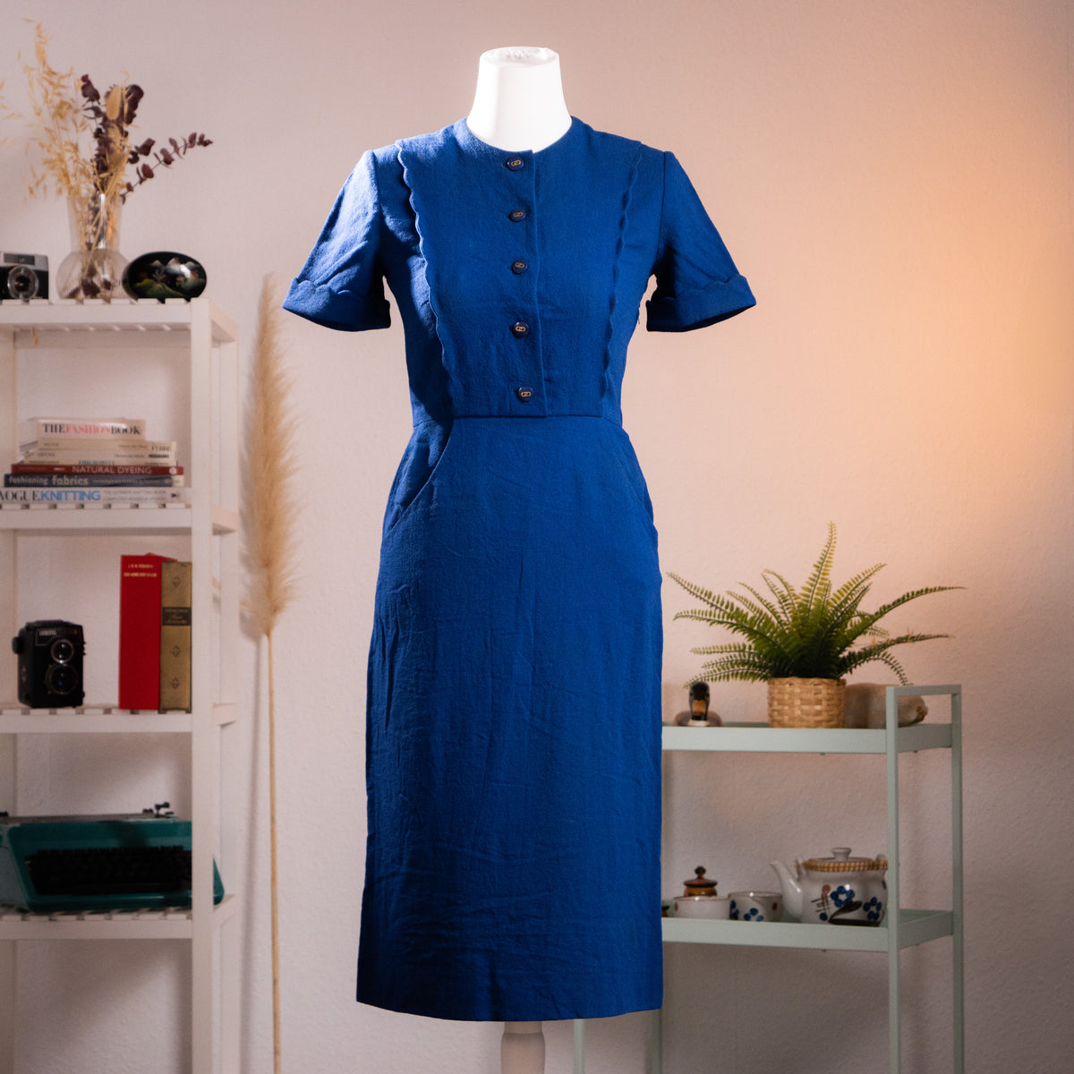 Archival Salvatore Ferragamo ultramarine blue wool crepe midi dress from the late 1970s with scalloped edges and logo buttons, front view on a gallery mannequin.

