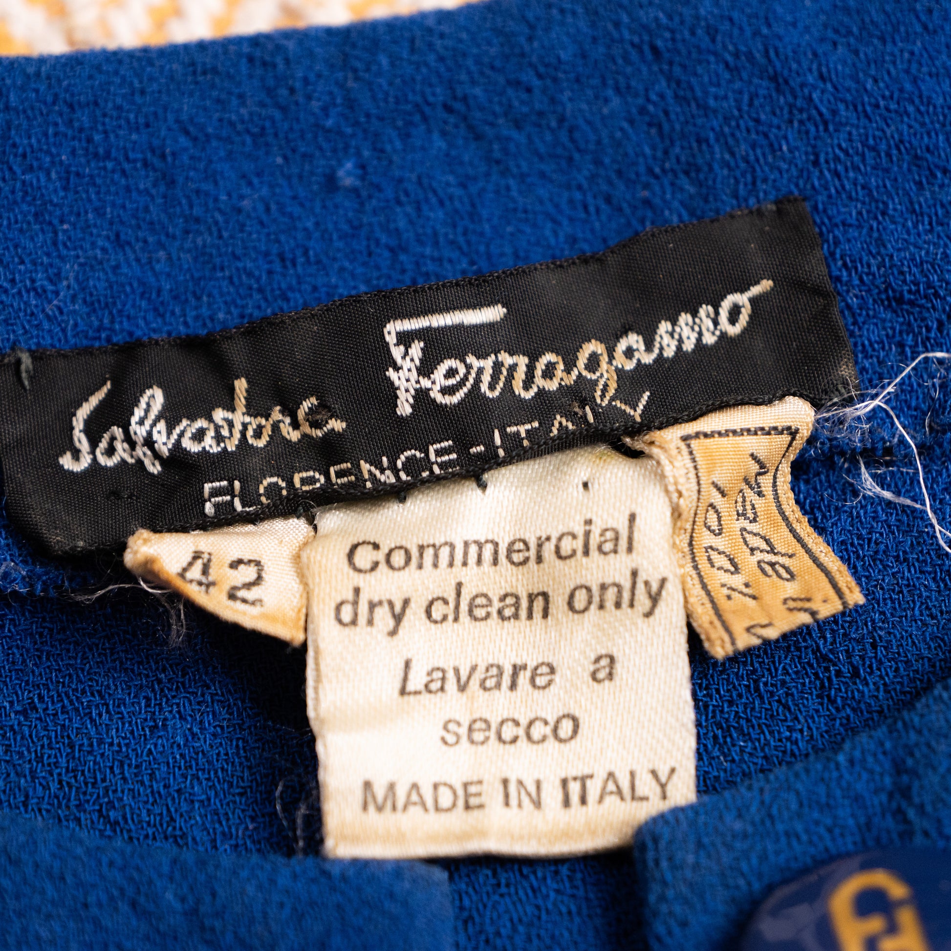 Close-up of the vintage Salvatore Ferragamo black woven satin neck label with size 42 and gold-braided 100 percent wool Made in Italy tag.
