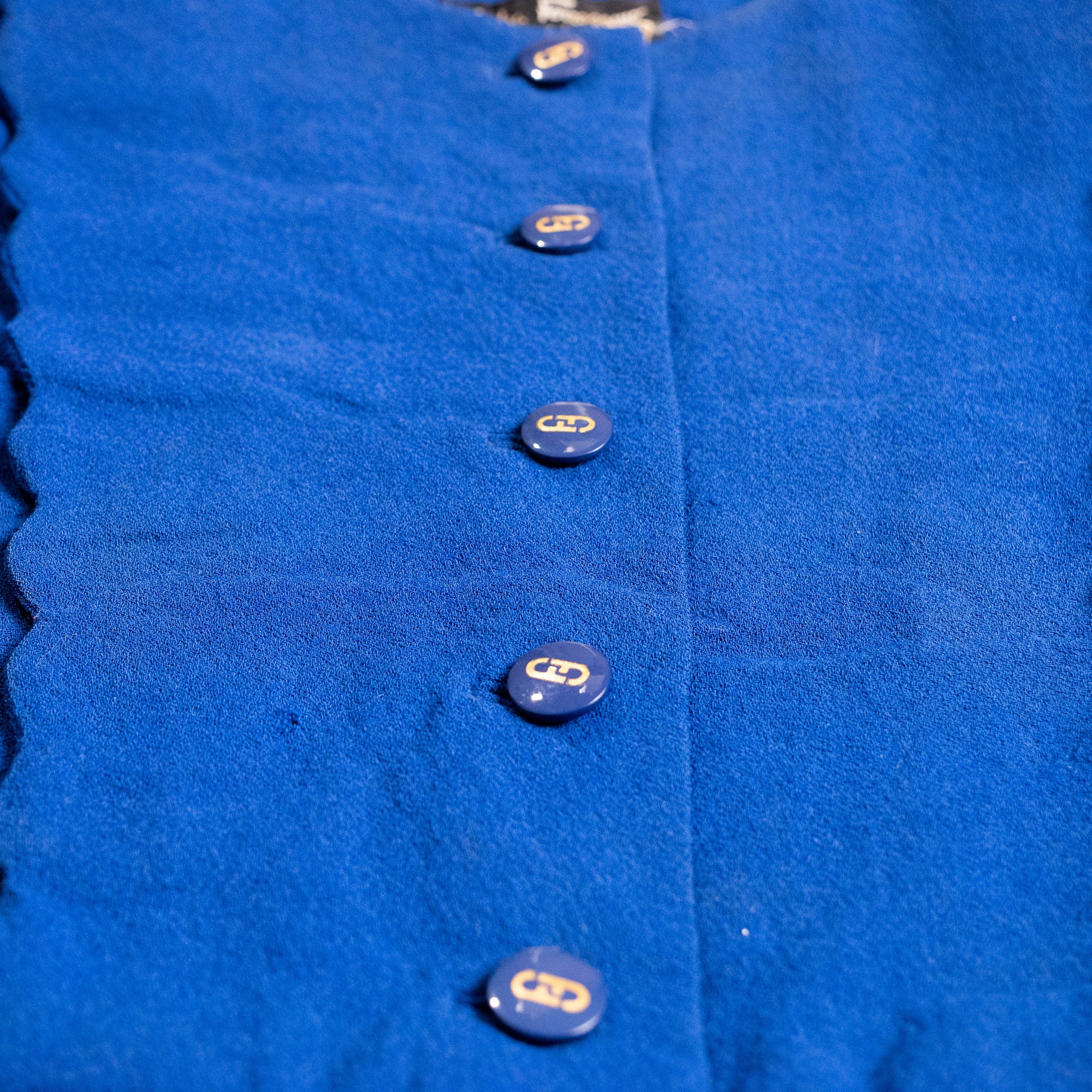 Macro shot of the original Salvatore Ferragamo navy blue resin buttons featuring the early metallic gold interlocking logo inlay.
