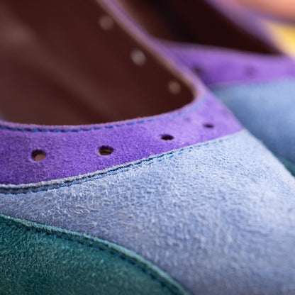 A close-up detail shot of the shoe's throat, showing the deep purple suede border accented by precision-punched wingtip brogue perforations. A portion of the interior leather lining is visible, stamped with a silver-foiled Miu Miu logo and "Made in Italy" inscription.