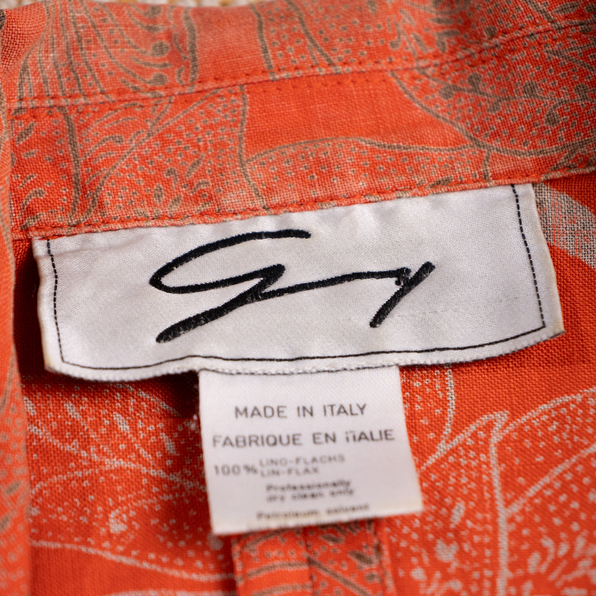 Close-up of the vintage archival Genny woven script neck label representing the Gianni Versace design era with 100 percent Lino-Flachs fabric tag.
