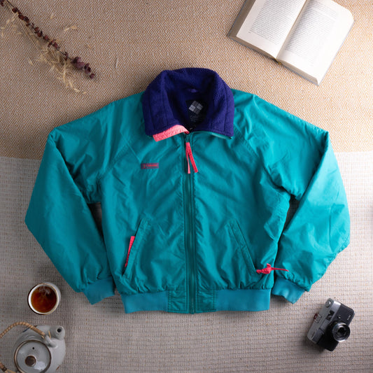 Vintage Columbia 80s–90s Fleece-Lined Bomber Jacket – teal nylon shell with navy blue sherpa fleece collar, hot pink contrast zip pull and pocket trim, full zip front, two zip hand pockets, ribbed hem and cuffs, gorpcore retro ski streetwear, Columbia logo patch at chest, flat lay editorial shot