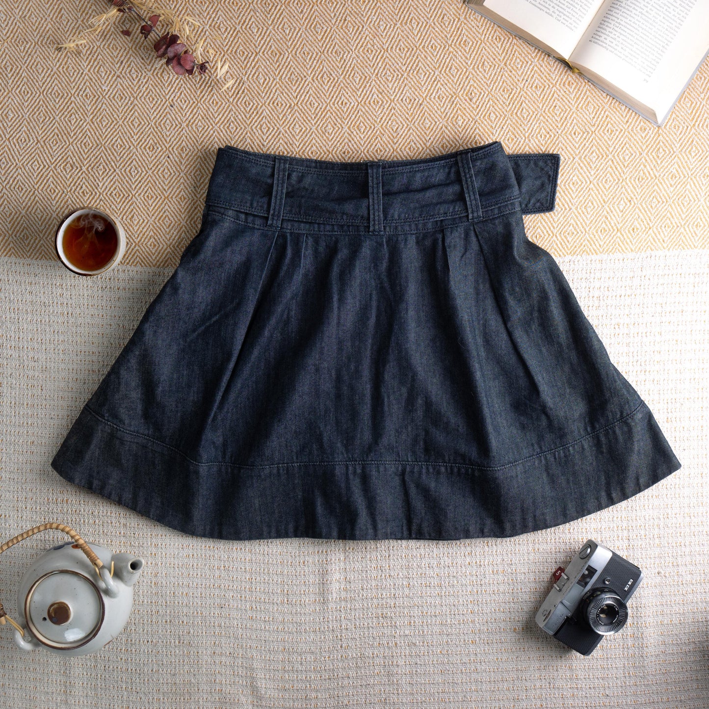 back view Miss Sixty Y2K Dark Wash Denim Pleated Skater Skirt – deep indigo dark wash denim, high waist with integrated belt and oversized silver Miss Sixty ring buckle, front box pleats, flared skater silhouette, horizontal seam panel at hem, side zip closure, preppy grunge schoolgirl aesthetic, flat lay editorial shot