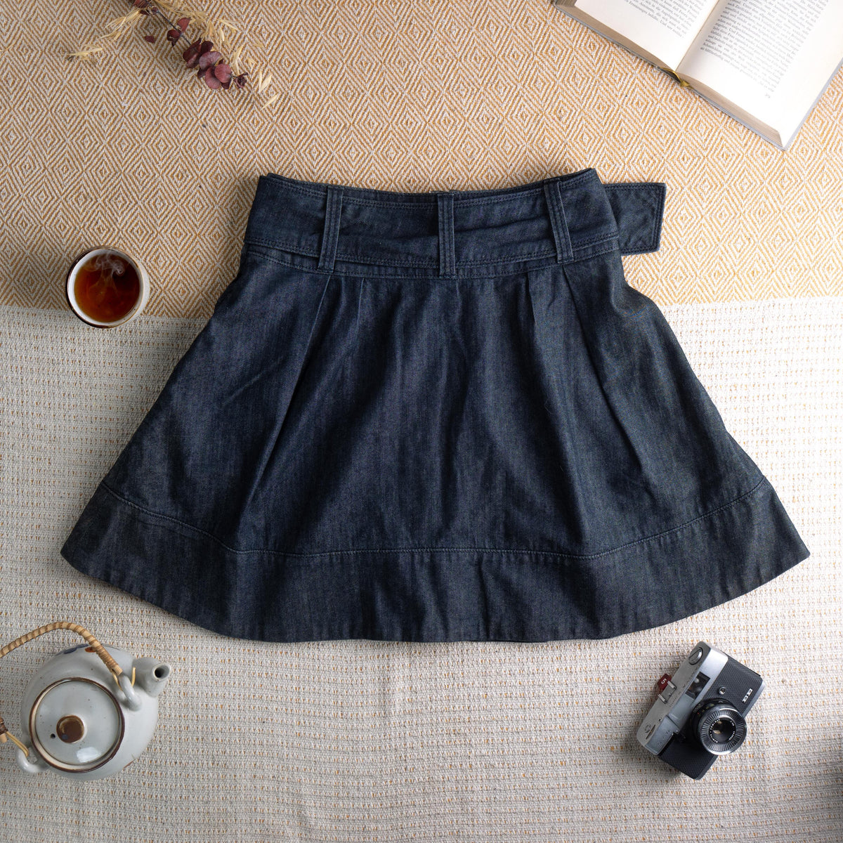 back view Miss Sixty Y2K Dark Wash Denim Pleated Skater Skirt – deep indigo dark wash denim, high waist with integrated belt and oversized silver Miss Sixty ring buckle, front box pleats, flared skater silhouette, horizontal seam panel at hem, side zip closure, preppy grunge schoolgirl aesthetic, flat lay editorial shot