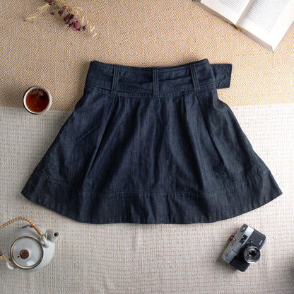 back view Miss Sixty Y2K Dark Wash Denim Pleated Skater Skirt – deep indigo dark wash denim, high waist with integrated belt and oversized silver Miss Sixty ring buckle, front box pleats, flared skater silhouette, horizontal seam panel at hem, side zip closure, preppy grunge schoolgirl aesthetic, flat lay editorial shot