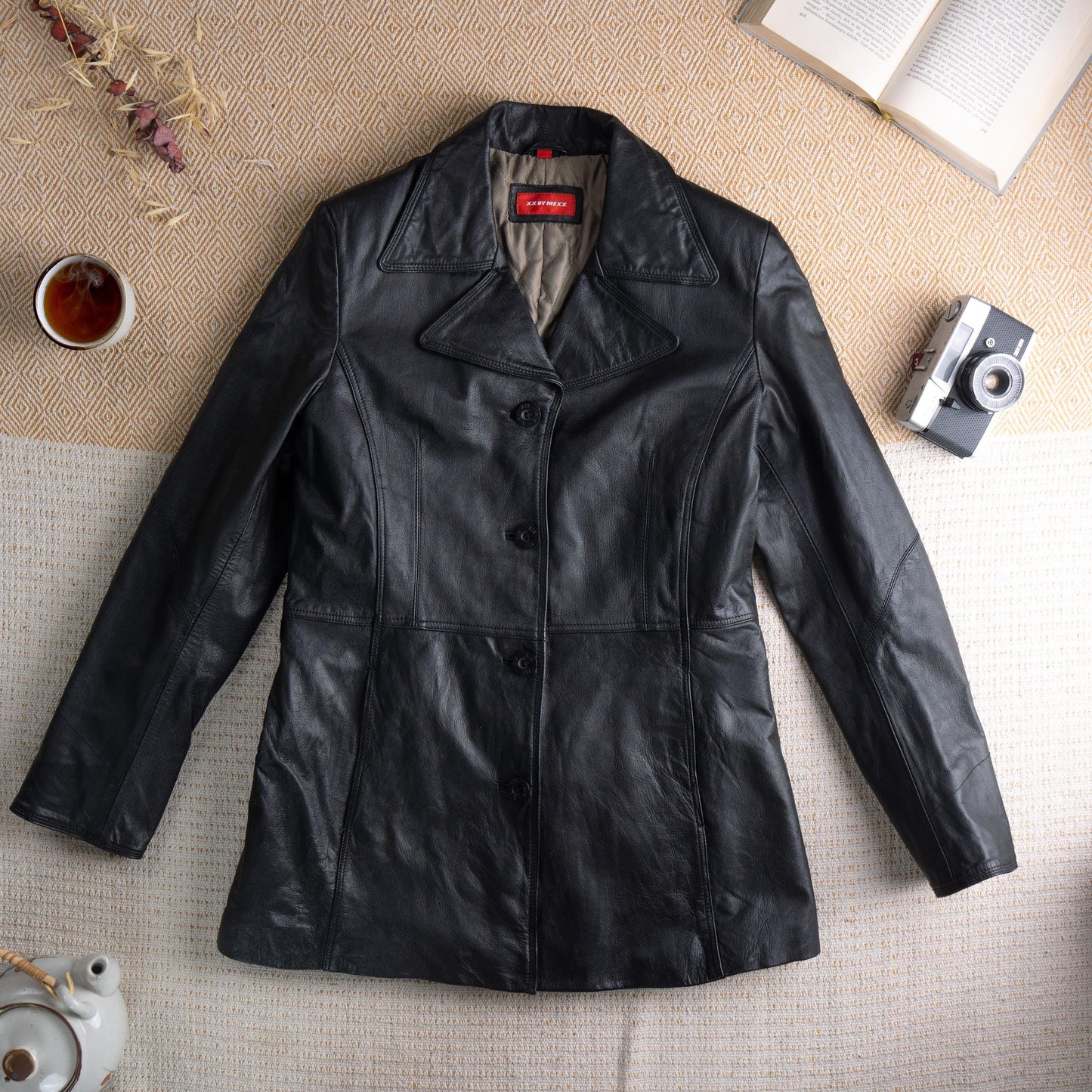 Deadstock XX by Mexx 90s Black Leather Longline Blazer – soft black genuine leather, wide notch lapel, three black button single-breasted front, princess seam panelling for fitted waist, two front hip pockets, quilted lining, long sleeves, minimalist matrix Y2K silhouette, red XX by Mexx label, flat lay editorial shot
