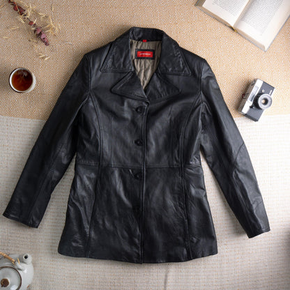 Deadstock XX by Mexx 90s Black Leather Longline Blazer – soft black genuine leather, wide notch lapel, three black button single-breasted front, princess seam panelling for fitted waist, two front hip pockets, quilted lining, long sleeves, minimalist matrix Y2K silhouette, red XX by Mexx label, flat lay editorial shot