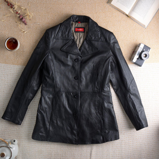 Deadstock XX by Mexx 90s Black Leather Longline Blazer – soft black genuine leather, wide notch lapel, three black button single-breasted front, princess seam panelling for fitted waist, two front hip pockets, quilted lining, long sleeves, minimalist matrix Y2K silhouette, red XX by Mexx label, flat lay editorial shot