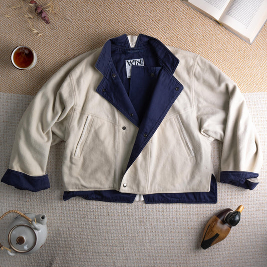 Rare WIN Line by Levi Strauss & Co. 80s Archival Cropped Boxy Jacket – off-white cream canvas body with contrasting navy blue collar, lapel, cuffs and hem trim, snap button front closure, two front patch pockets with snap buttons, oversized boxy silhouette, WIN by Levi's label, Made in Belgium, flat lay editorial shot