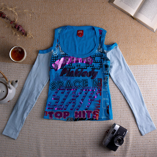 Miss Sixty Y2K Archive Cold Shoulder Metallic Foil Graphic Top – turquoise blue stretch jersey body with all-over metallic pink and purple foil disco typography print reading "Top Hits", "Space M", "Pink Lady", cold shoulder cut-out with attached pale blue long sleeves, scoop neckline, layered effect, cyber Y2K grunge, Made in Italy, flat lay editorial shot