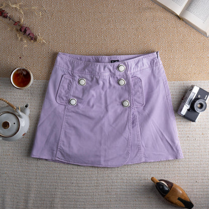 Vintage D&G Dolce & Gabbana Y2K Lavender Mini Skirt – soft lilac pastel cotton twill, low rise A-line silhouette, double-breasted front with six large silver dome buttons, two front patch pockets, D&G logo tab at waistband, back zip closure, preppy coquette 2000s aesthetic, flat lay editorial shot