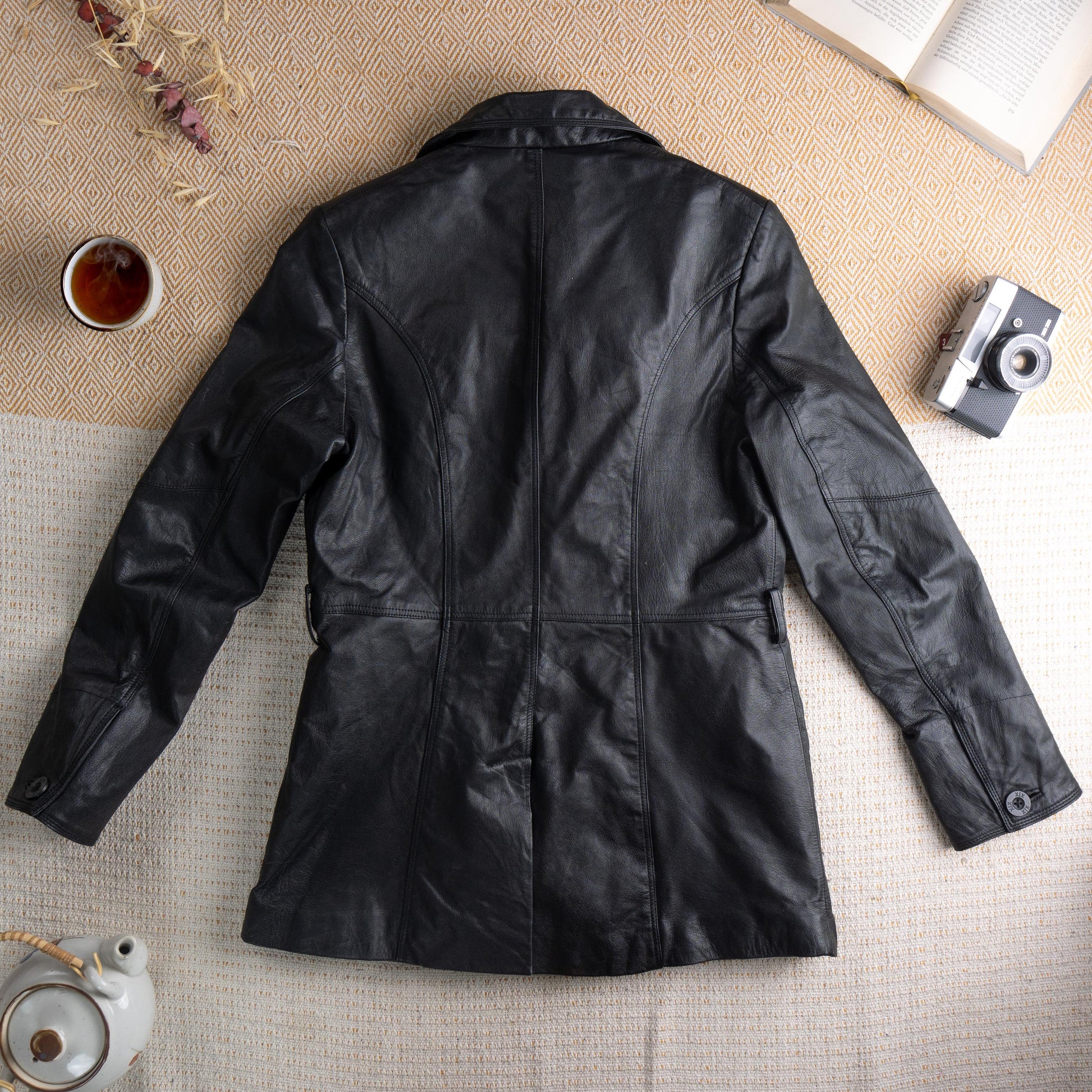 back view Deadstock XX by Mexx 90s Black Leather Longline Blazer – soft black genuine leather, wide notch lapel, three black button single-breasted front, princess seam panelling for fitted waist, two front hip pockets, quilted lining, long sleeves, minimalist matrix Y2K silhouette, red XX by Mexx label, flat lay editorial shot
