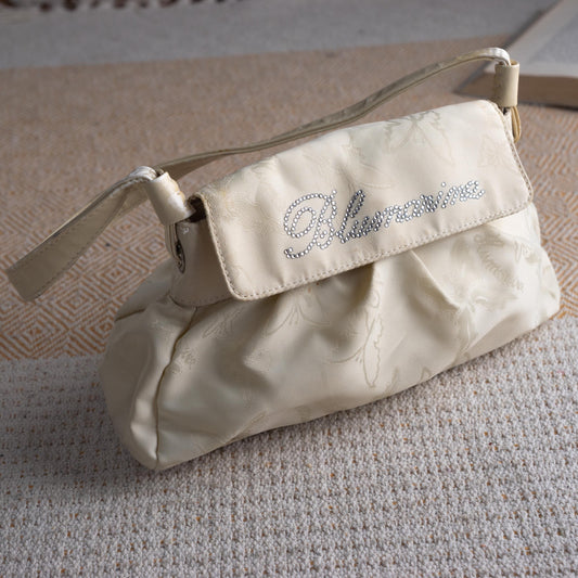 Vintage Blumarine Y2K Cream Jacquard Baguette Shoulder Bag – ivory cream tonal butterfly jacquard fabric, gathered ruched body, structured flap with rhinestone crystal "Blumarine" script logo, single flat leather shoulder strap with gold hardware snap closure, Made in Italy, fairycore coquette aesthetic, product shot on textured surface