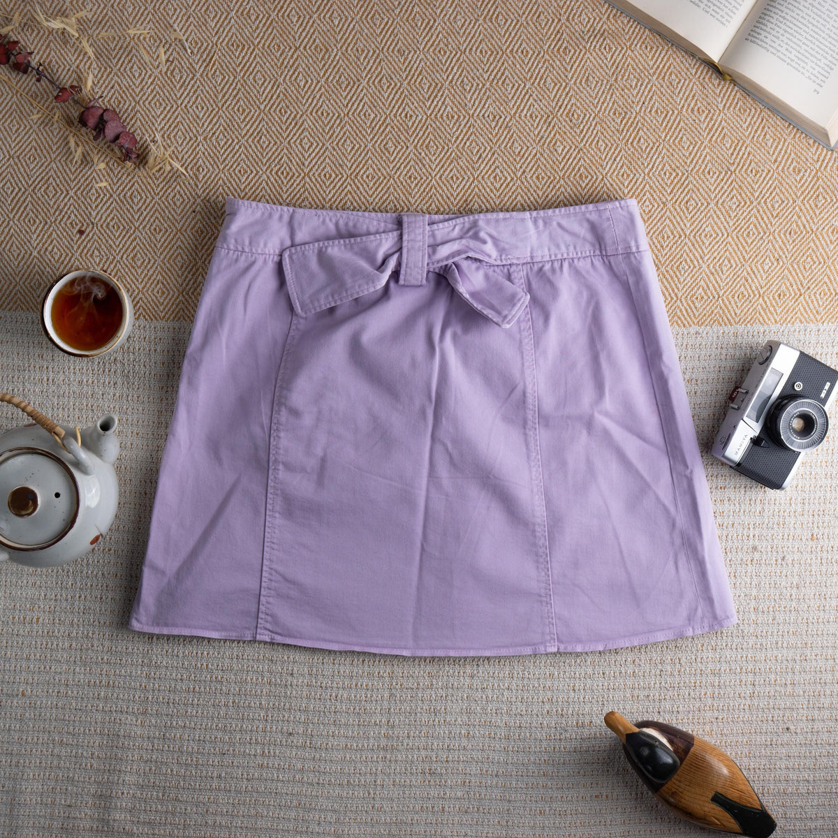 back view Vintage D&G Dolce & Gabbana Y2K Lavender Mini Skirt – soft lilac pastel cotton twill, low rise A-line silhouette, double-breasted front with six large silver dome buttons, two front patch pockets, D&G logo tab at waistband, back zip closure, preppy coquette 2000s aesthetic, flat lay editorial shot