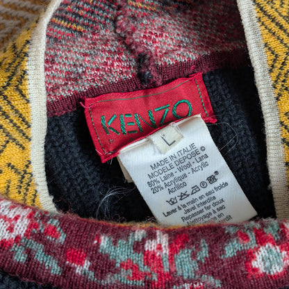 Close-up of a Kenzo label on a patterned garment with care . Archival Kenzo Paris 90s Floral Patchwork Ribbed Knit Crop Sweater – charcoal grey wide-rib knit body with cobalt blue lurex pointelle shoulder panels, multicolour patchwork long sleeves featuring folk floral, cherry, geometric diamond and stripe jacquard bands in red, blue, yellow and black, contrast burgundy and yellow folk-print turtleneck collar, boxy cropped silhouette, Takada era, Made in Italy, product shot on dress forminstructions.
