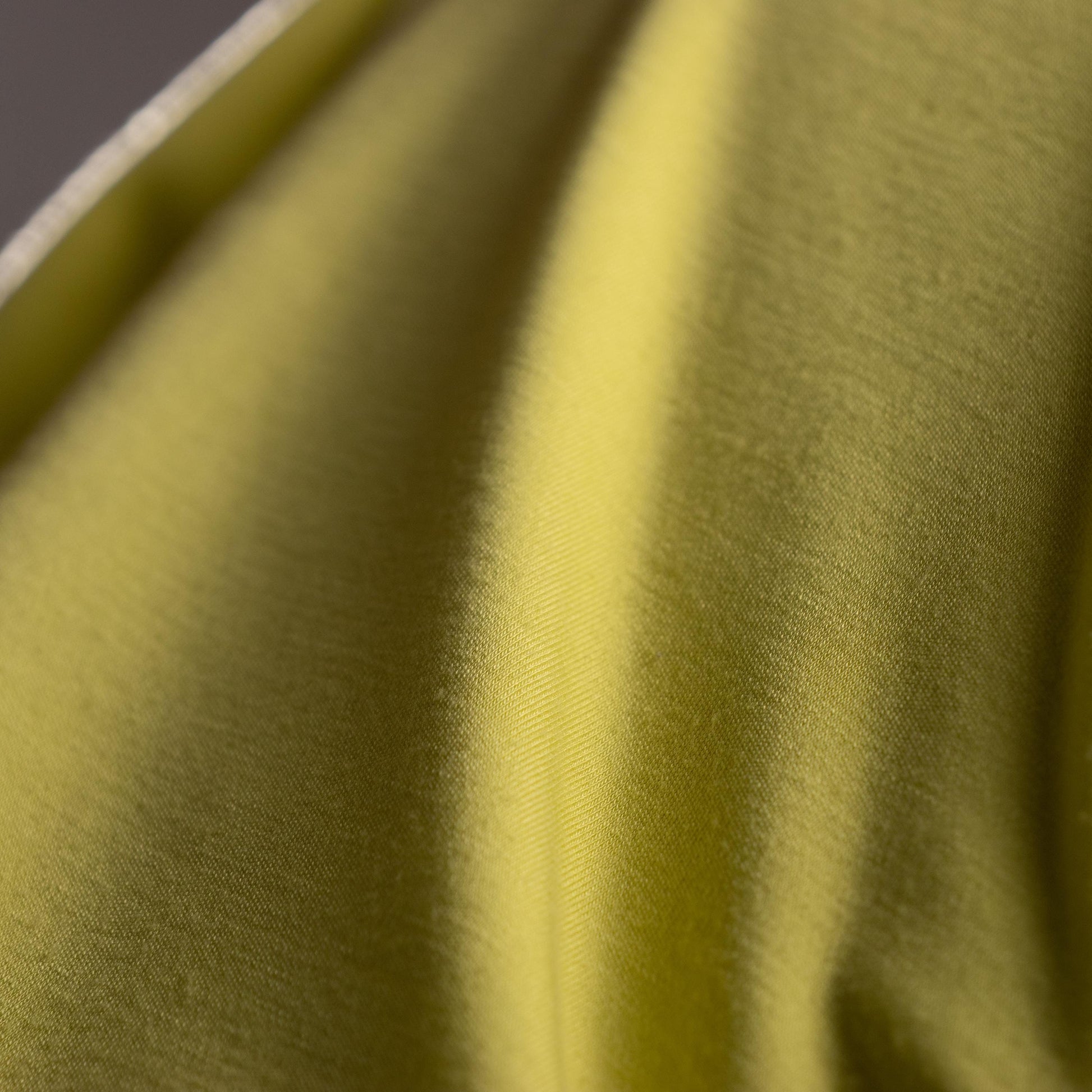 Close-up of green fabric with a subtle pattern. Archival Halston Mainline 2000s Acid Lime Asymmetric Off-Shoulder Mini Dress – saturated acid lime yellow-green stretch satin, single asymmetric diagonal off-shoulder neckline, one long sleeve, body-con mini silhouette, silk lining, Bradley Bayou era, Made in Italy IT 38 XS S, product shot on dress form
