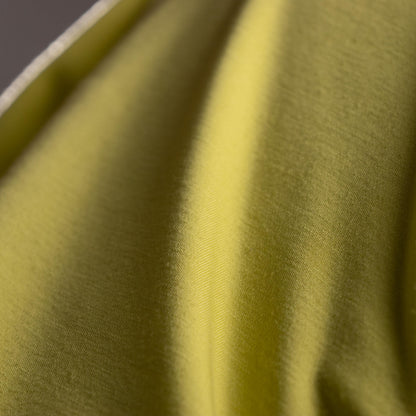 Close-up of green fabric with a subtle pattern. Archival Halston Mainline 2000s Acid Lime Asymmetric Off-Shoulder Mini Dress – saturated acid lime yellow-green stretch satin, single asymmetric diagonal off-shoulder neckline, one long sleeve, body-con mini silhouette, silk lining, Bradley Bayou era, Made in Italy IT 38 XS S, product shot on dress form