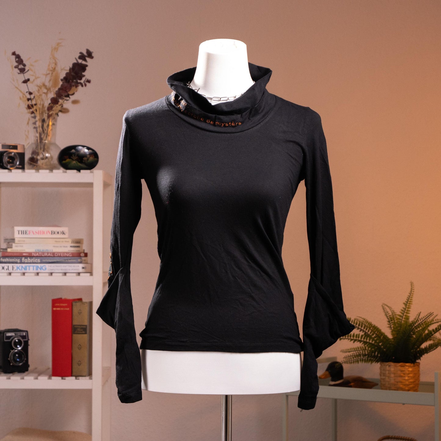 Rare Archival Cop Copine "Gridley" 90s Deconstructed Noir Top – jet black stretch jersey, asymmetric draped cowl turtleneck with red "c de mystère" embroidered text at collar, silver hardware buckle detail at neck and cuffs, long sleeves with open split cuff, fitted silhouette, French avant-garde minimalist cyber, product shot on dress form