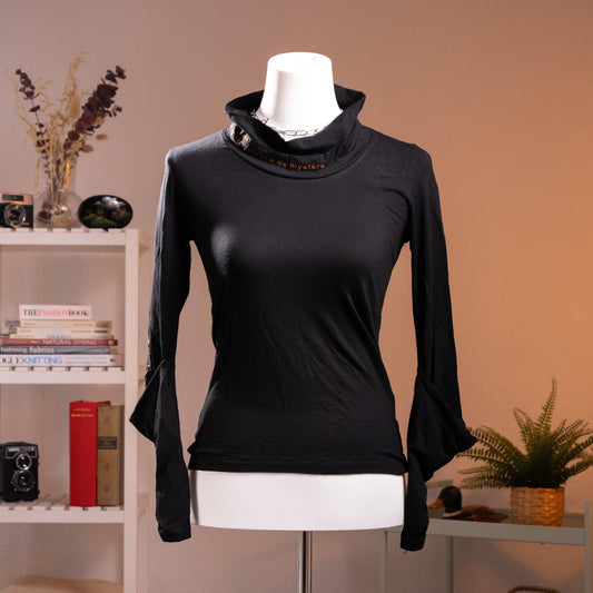 Rare Archival Cop Copine "Gridley" 90s Deconstructed Noir Top – jet black stretch jersey, asymmetric draped cowl turtleneck with red "c de mystère" embroidered text at collar, silver hardware buckle detail at neck and cuffs, long sleeves with open split cuff, fitted silhouette, French avant-garde minimalist cyber, product shot on dress form
