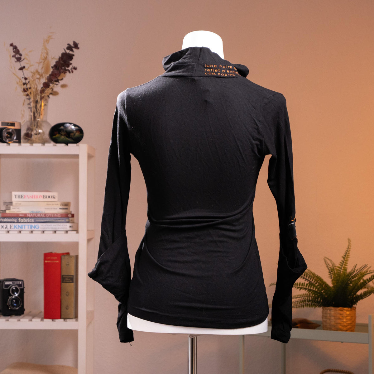back view Rare Archival Cop Copine "Gridley" 90s Deconstructed Noir Top – jet black stretch jersey, asymmetric draped cowl turtleneck with red "c de mystère" embroidered text at collar, silver hardware buckle detail at neck and cuffs, long sleeves with open split cuff, fitted silhouette, French avant-garde minimalist cyber, product shot on dress form
