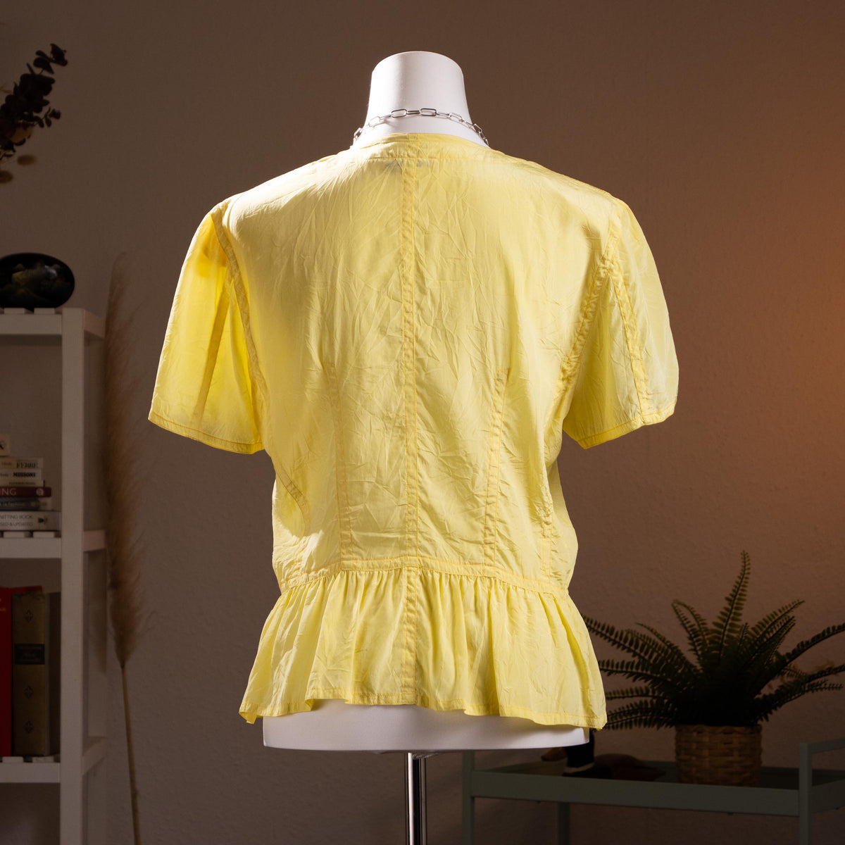 back view Jil Sander Plus Crinkle Silk Peplum Blouse – citrine yellow crinkled silk, round neckline, short puff sleeves, mother-of-pearl button-front, fitted waist with flared peplum hem, quiet luxury modern archive aesthetic, Lucie and Luke Meier era, product shot on dress form