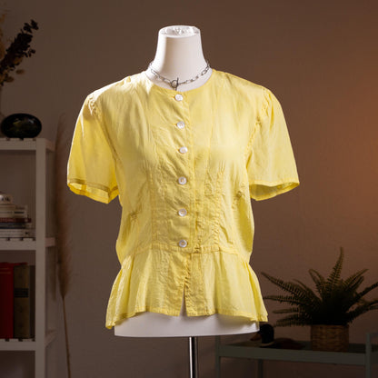 Jil Sander Plus Crinkle Silk Peplum Blouse – citrine yellow crinkled silk, round neckline, short puff sleeves, mother-of-pearl button-front, fitted waist with flared peplum hem, quiet luxury modern archive aesthetic, Lucie and Luke Meier era, product shot on dress form