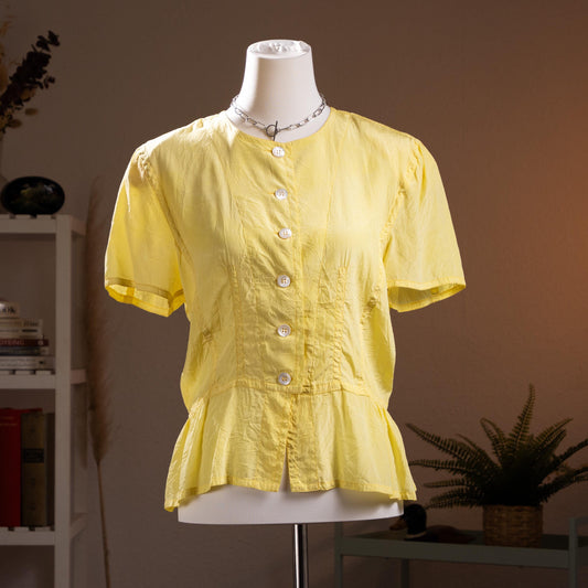 Jil Sander Plus Crinkle Silk Peplum Blouse – citrine yellow crinkled silk, round neckline, short puff sleeves, mother-of-pearl button-front, fitted waist with flared peplum hem, quiet luxury modern archive aesthetic, Lucie and Luke Meier era, product shot on dress form