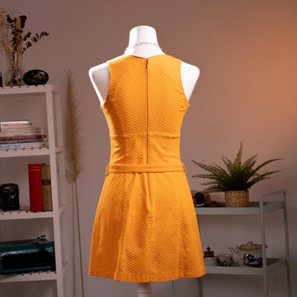 back view Archival Iceberg Jeans 90s Mod Revival Mini Dress – saffron yellow textured cotton piqué, deep V-neckline, sleeveless, A-line silhouette with double silver ring-buckle self-belt at waist, mod retro aesthetic, product shot on dress form