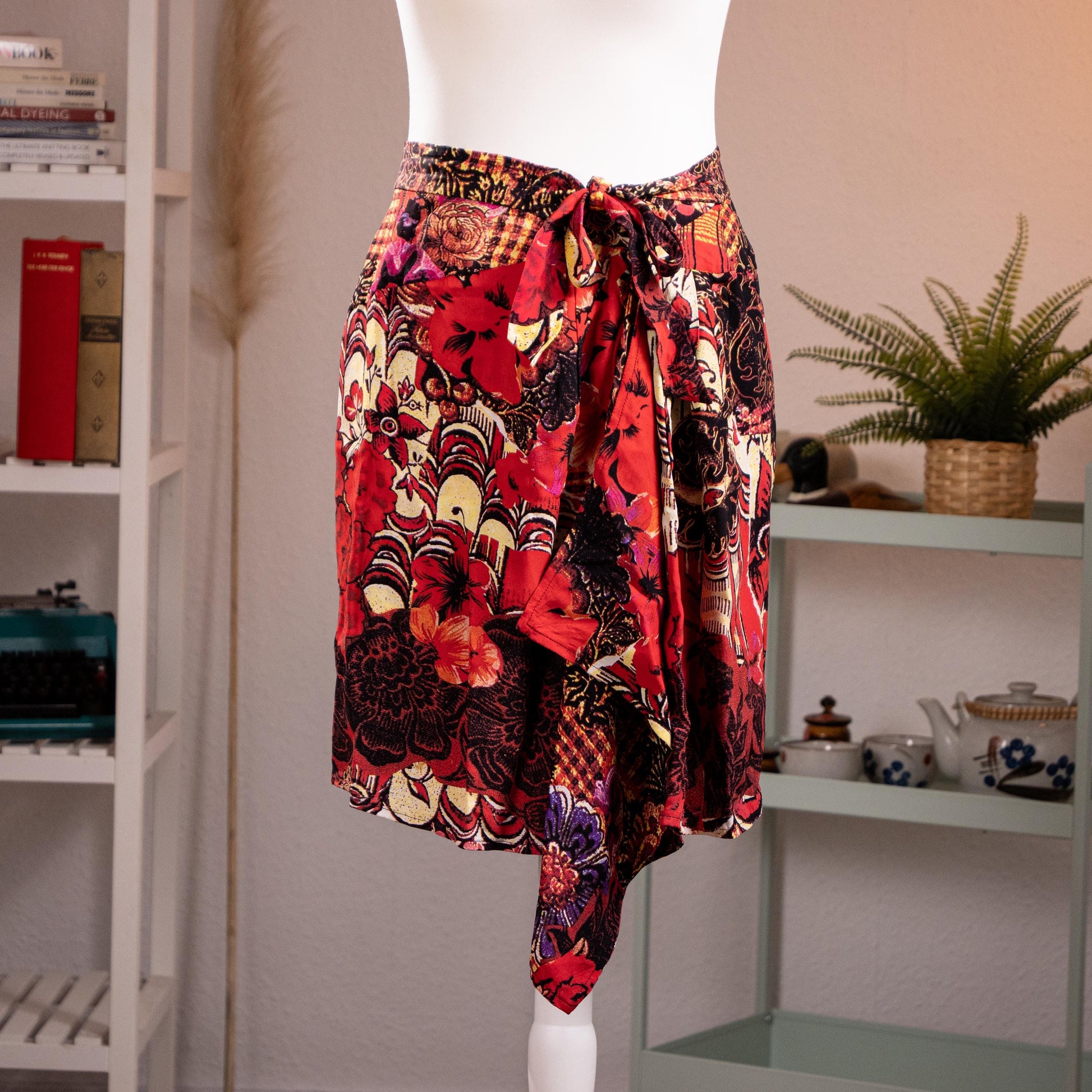Archival Christian Lacroix FW96 Deadstock Asymmetric Wrap Skirt – bold maximalist floral print in crimson red, black, gold and purple on silk-feel fabric, self-tie bow waist, dramatic asymmetric handkerchief hem, product shot on dress form