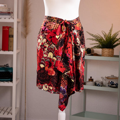 Archival Christian Lacroix FW96 Deadstock Asymmetric Wrap Skirt – bold maximalist floral print in crimson red, black, gold and purple on silk-feel fabric, self-tie bow waist, dramatic asymmetric handkerchief hem, product shot on dress form