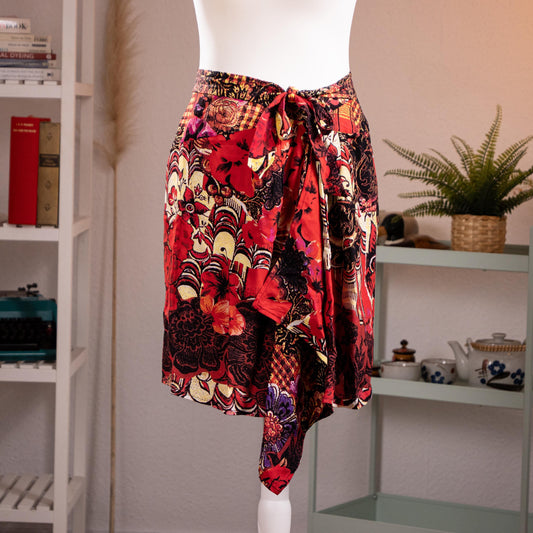 Archival Christian Lacroix FW96 Deadstock Asymmetric Wrap Skirt – bold maximalist floral print in crimson red, black, gold and purple on silk-feel fabric, self-tie bow waist, dramatic asymmetric handkerchief hem, product shot on dress form